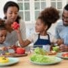 A happy young family with two little kids prepare a healthy salad by chopping up lettuce, tomatoes, and peppers.