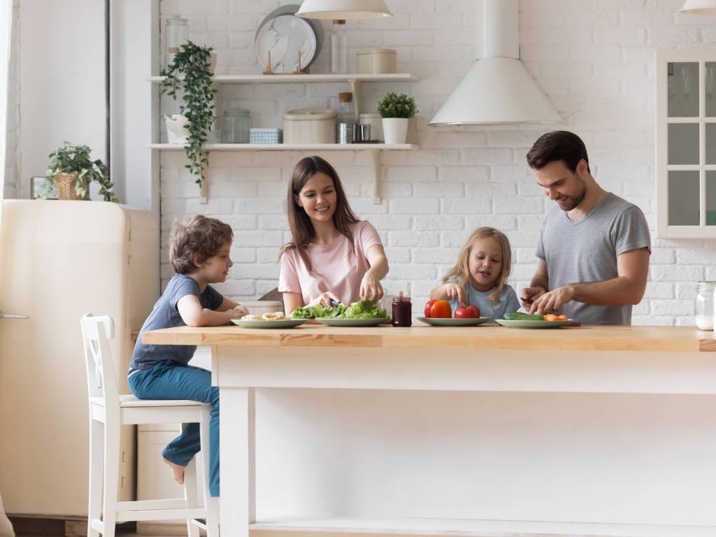 A happy family of four at the kitchen island enjoying a meal together. There is one kid sitting next to each parent.