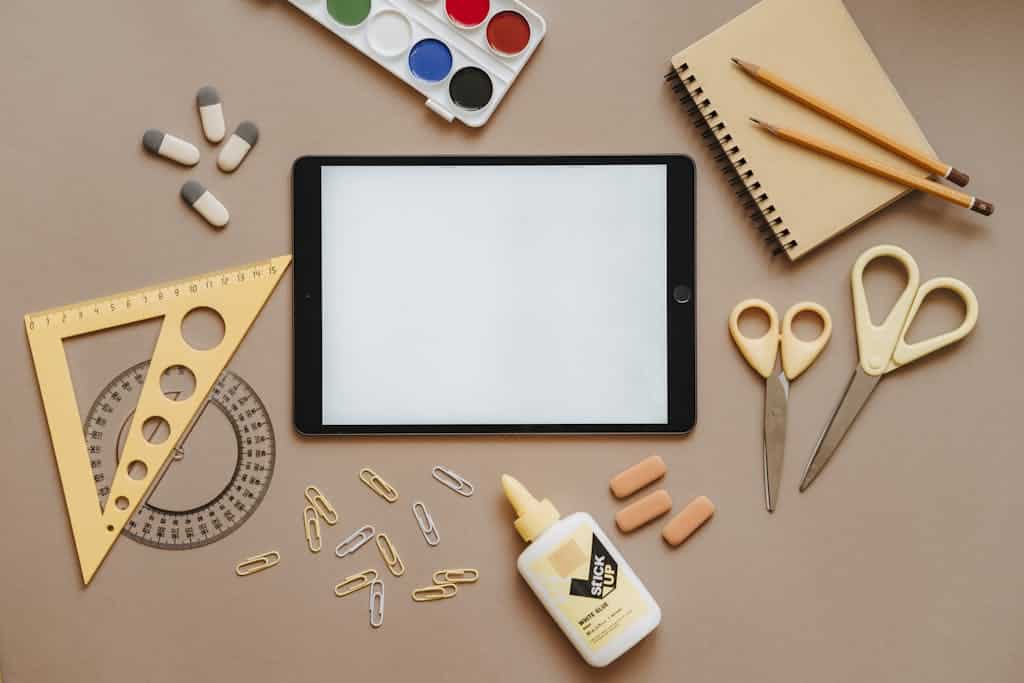 Flat lay of school supplies including tablet, scissors, glue, and stationery. Ideal for education themes.