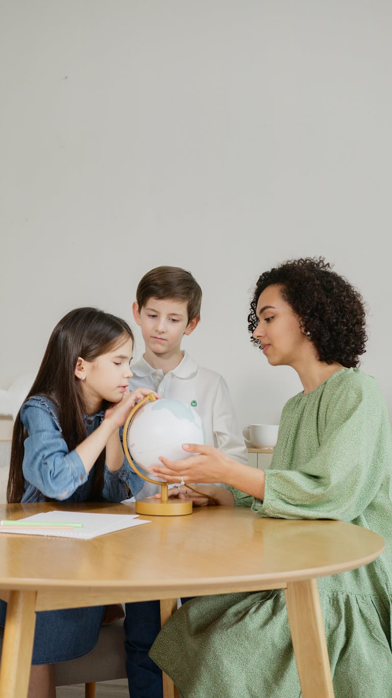 Teacher guiding children using a globe for geography lesson indoors.