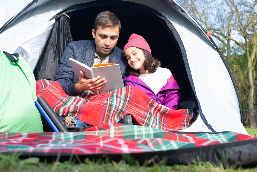 Father and daughter enjoy reading together in a cozy tent, capturing a moment of bonding in nature.