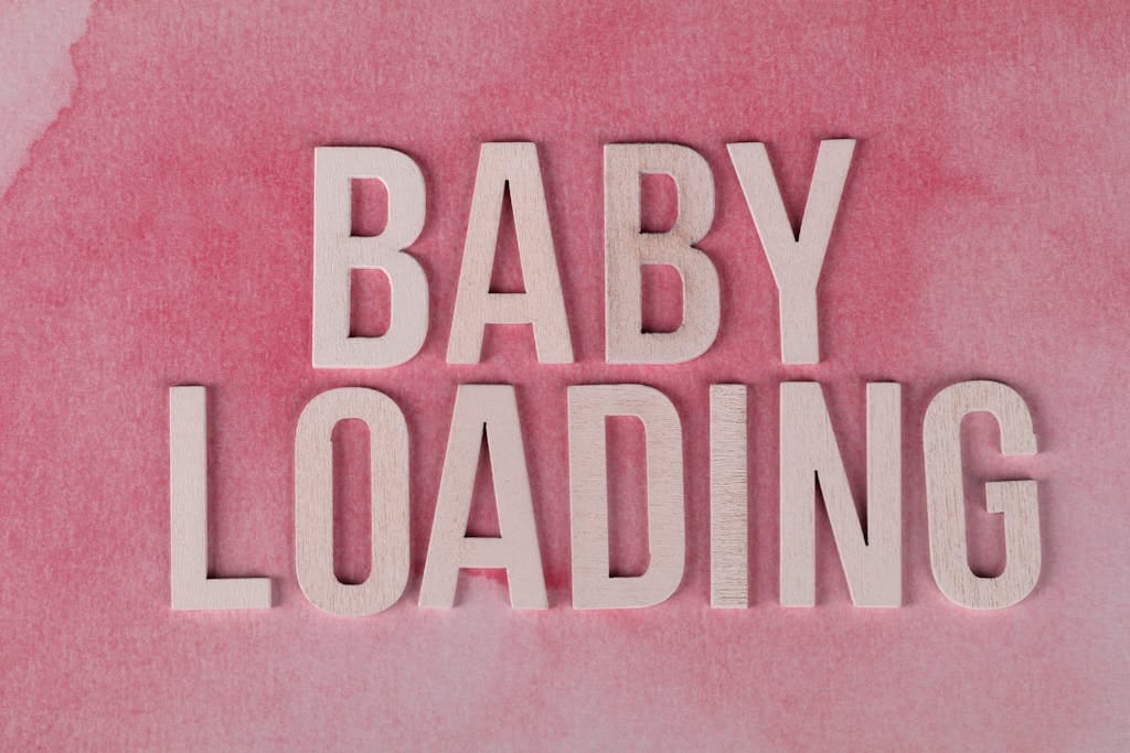 Close-up of 'Baby Loading' text in wooden letters on a pink watercolor background.
