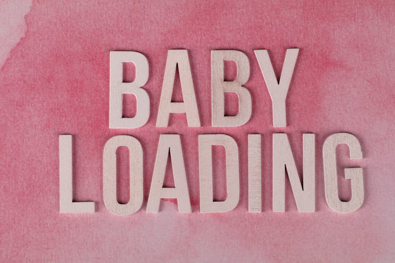 Close-up of 'Baby Loading' text in wooden letters on a pink watercolor background.