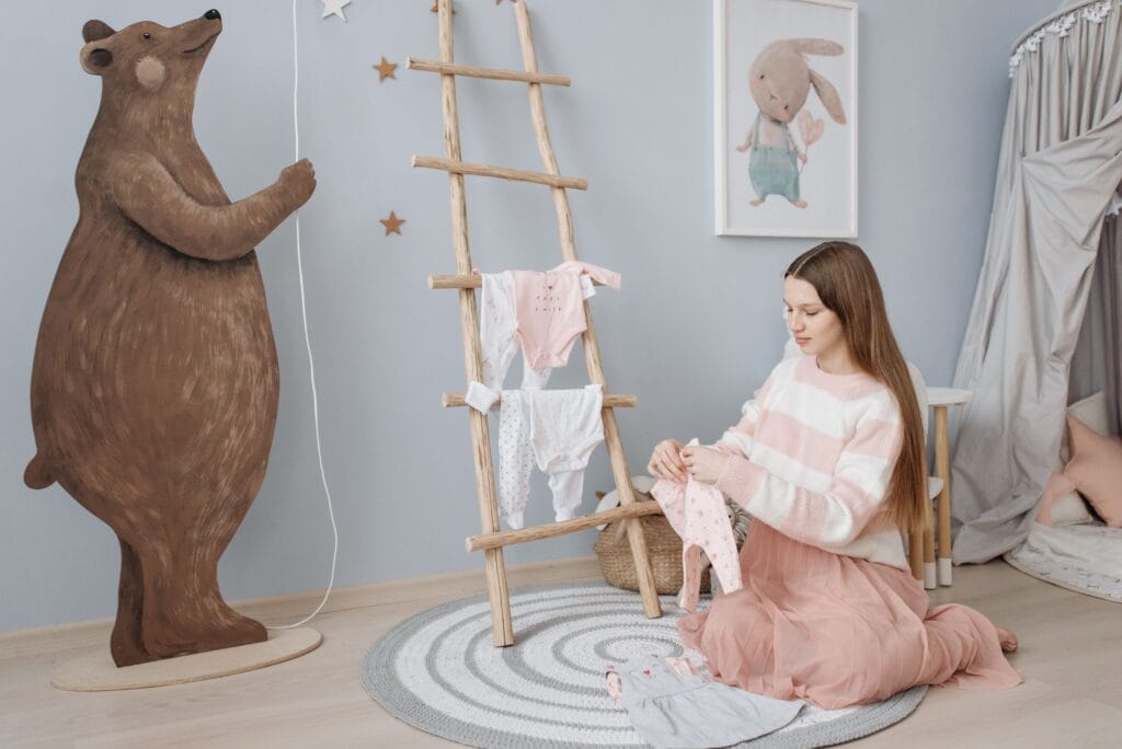 A pregnant woman sits on the floor folding baby clothes in a beautifully decorated nursery.
