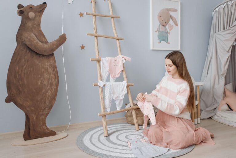 A pregnant woman sits on the floor folding baby clothes in a beautifully decorated nursery.