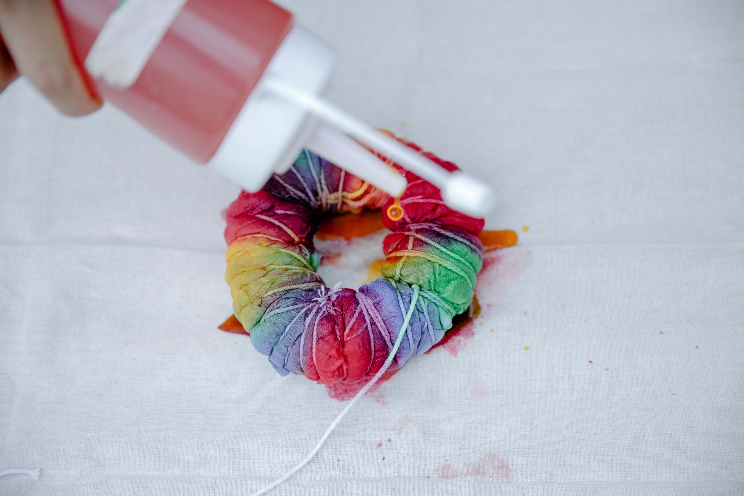 From above of faceless artisan with squeeze bottle painting colorful fabric tied with threads while demonstrating tie dye technique on white background