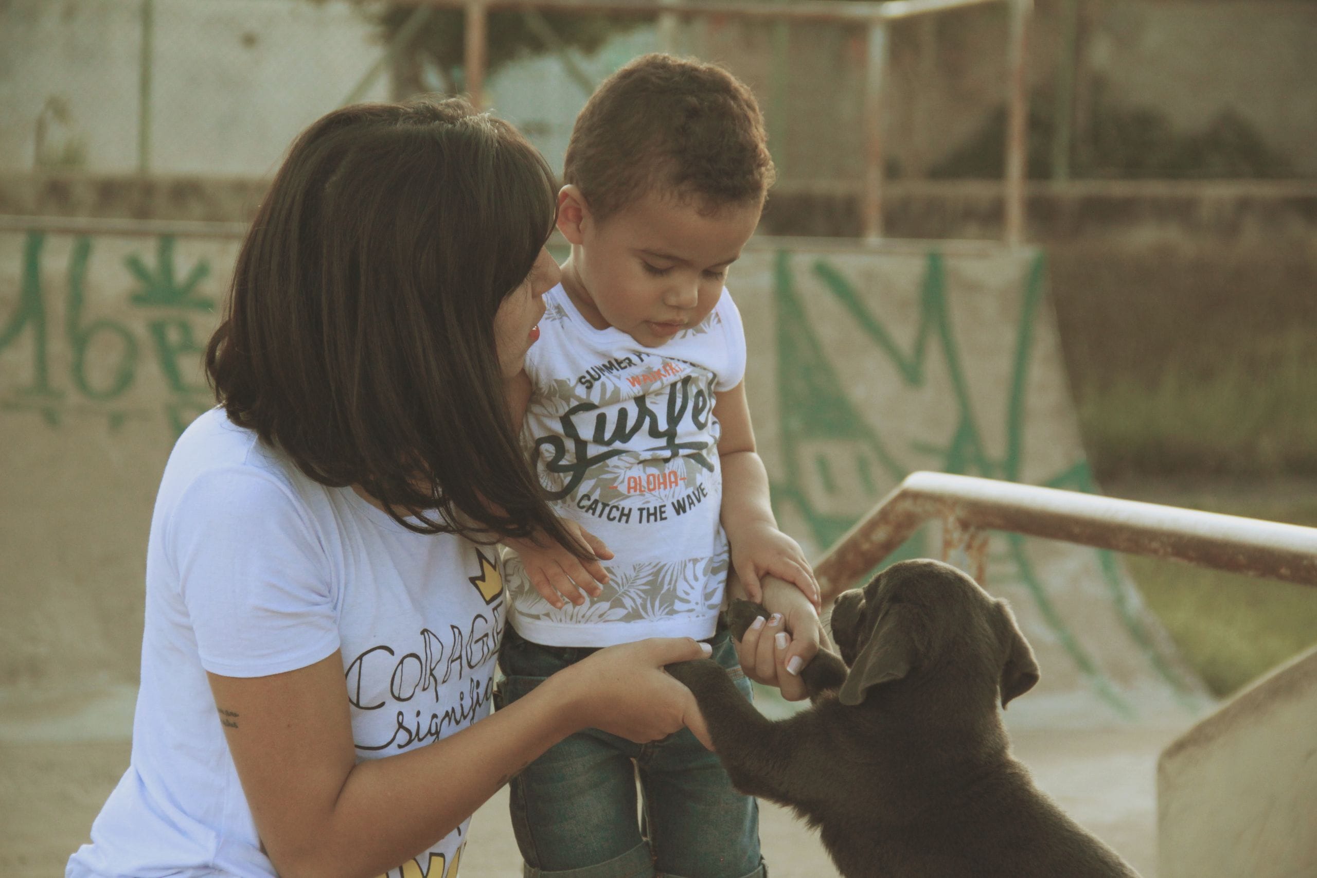 A loving moment between a mother, her child, and a playful puppy captured in an outdoor setting, evoking togetherness.
