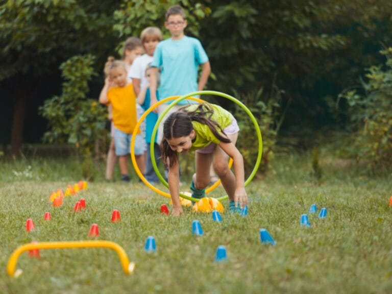 A young girl moving through hoops in an outdoor obstacle course. There are several children lined up behind her.