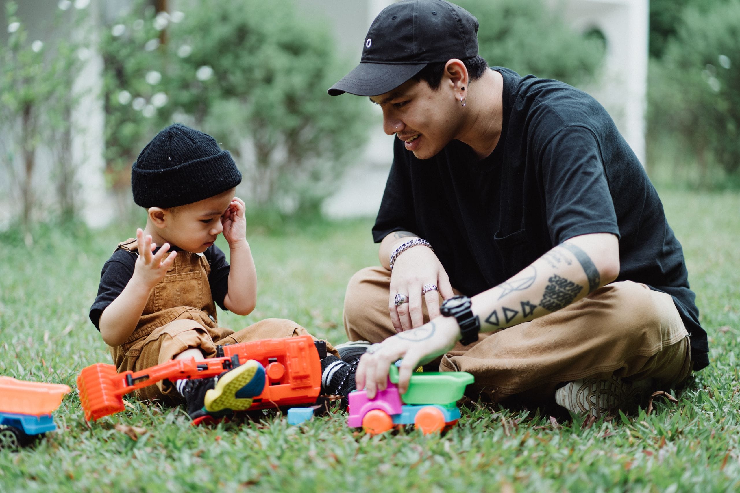 A father and son playing with toy trucks on the grass, sharing moments of joy and bonding.
