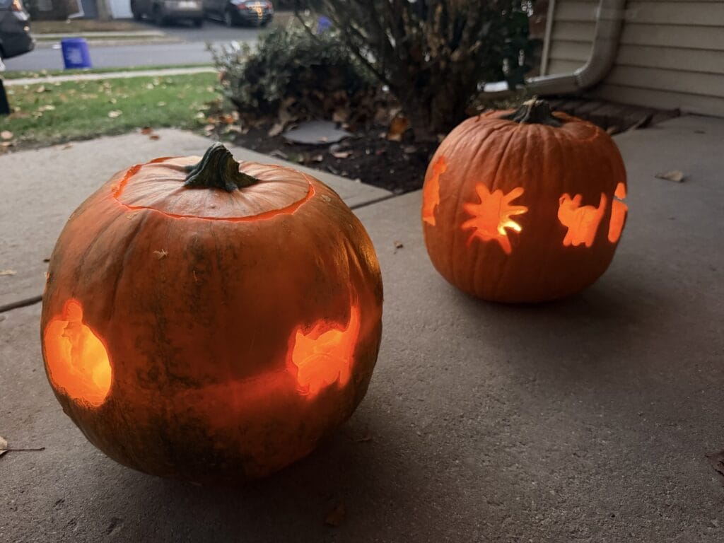 Two glowing jack-o'-lanterns with creative carved designs displayed outdoors at night.