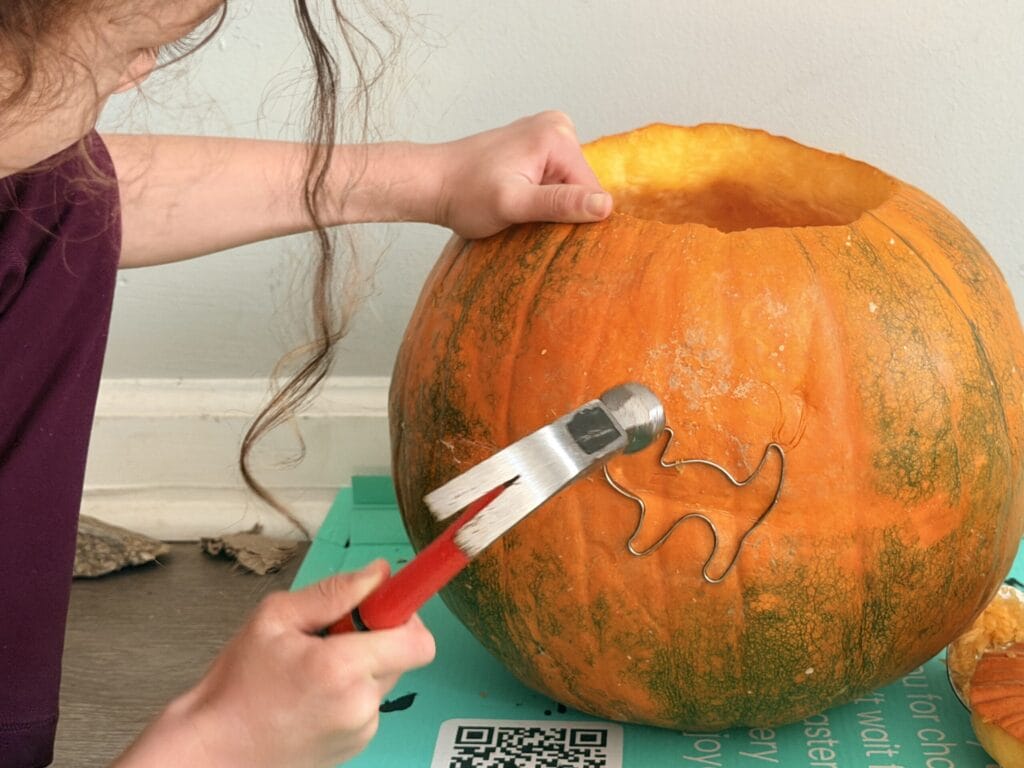 Child using a hammer and metal cookie cutter to create a design in a pumpkin.
