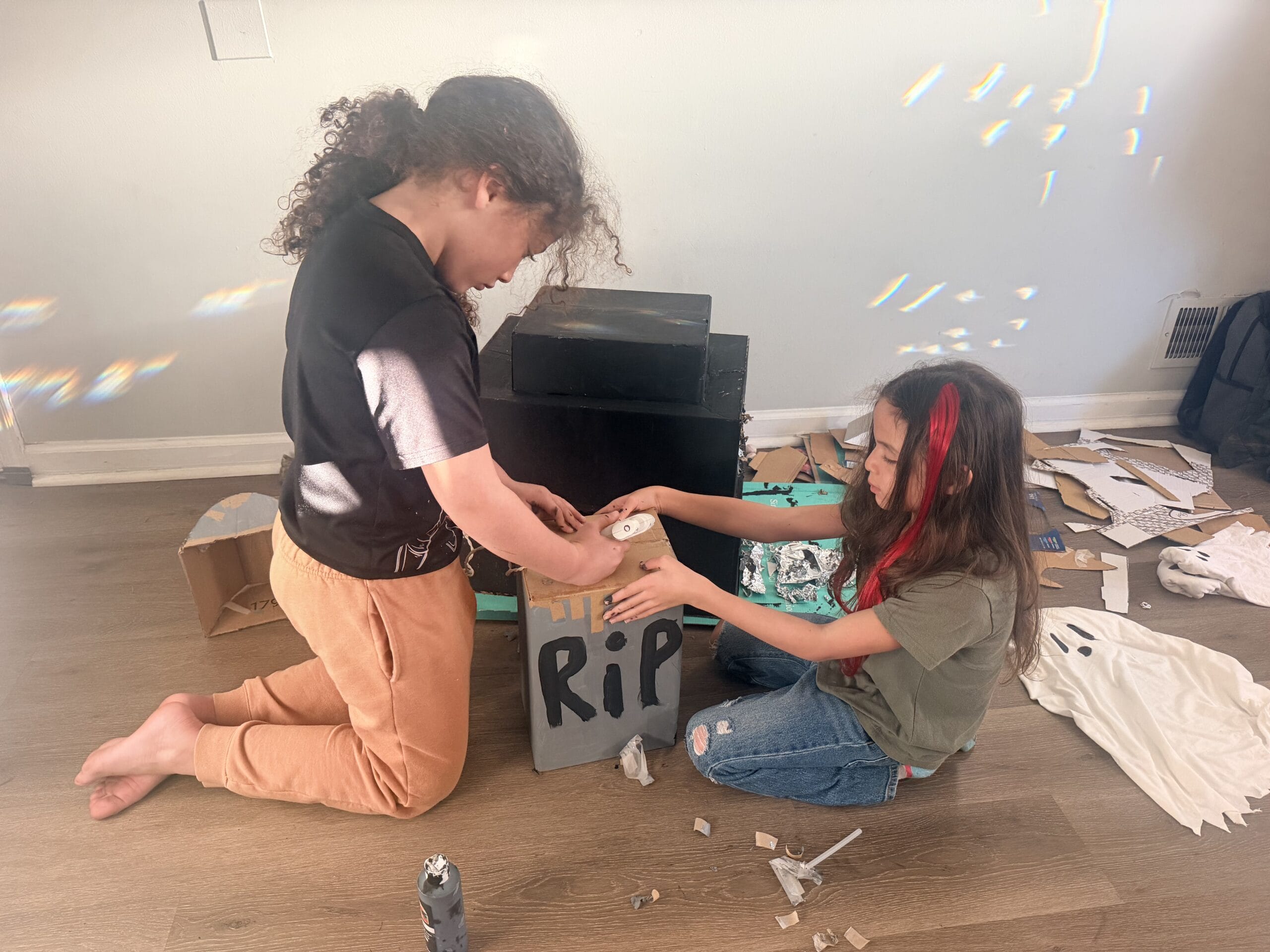 Kids painting and decorating a homemade cardboard Halloween tombstone.