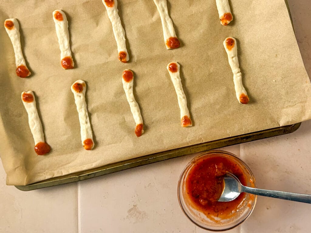 Finger-shaped pizza dough arranged on a baking sheet with marinara sauce on the ends.