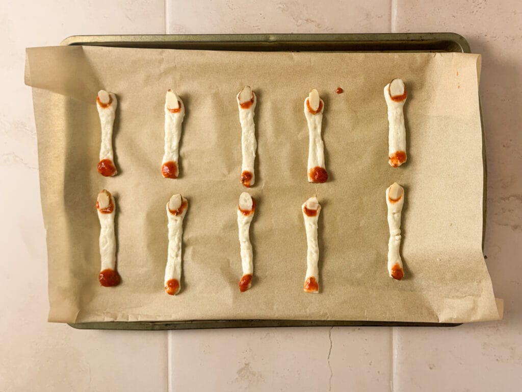 Unbaked Halloween finger breadsticks with sliced almond fingernails and marinara sauce.