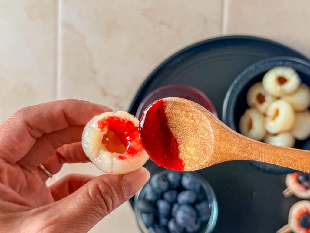 Adding red strawberry jelly to a canned lychee to make a bloody Halloween eyeball.
