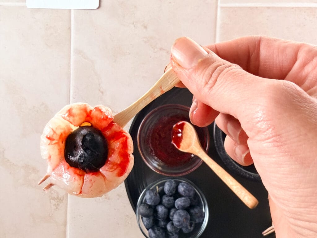 Spooky lychee eyeball with a blueberry center served on a mini wooden fork.
