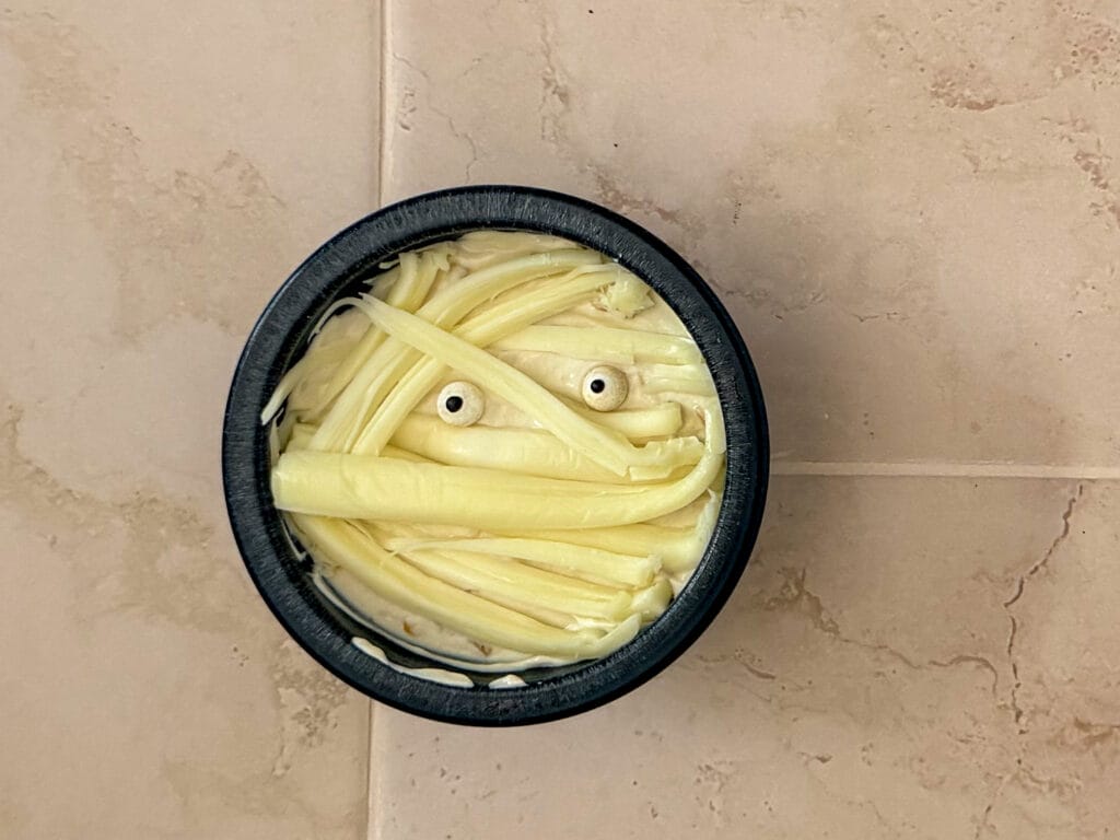 Finished Halloween mummy dip decorated with string cheese bandages and candy eyes.