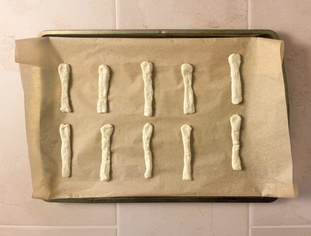 Finger-shaped pizza dough strips arranged on a parchment-lined baking sheet to make Halloween breadstick fingers.