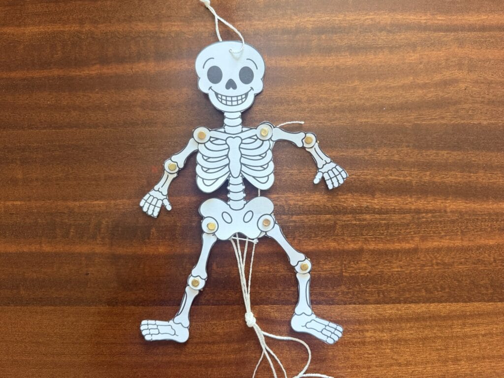 Completed paper dancing skeleton craft hanging by a string with pull strings attached to move its arms and legs.