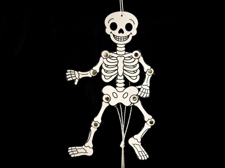 Finished glow-in-the-dark dancing skeleton craft hanging against a black background with movable arms and legs.